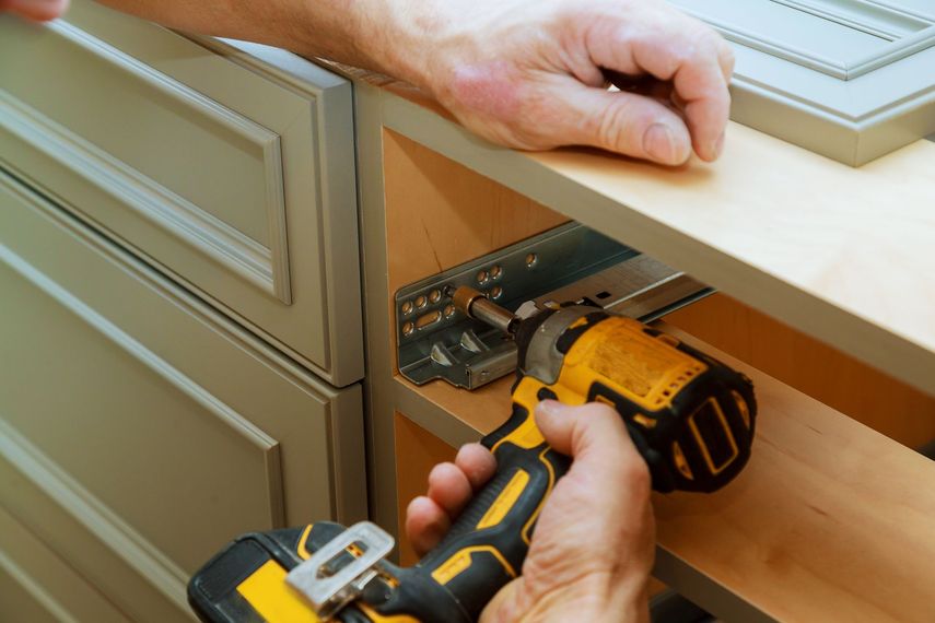 A man is using a drill to install a drawer in a kitchen.