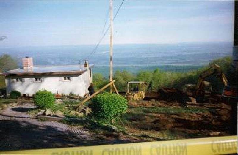 Construction site with a small building, tall pole, and heavy machinery, overlooking a distant vista.