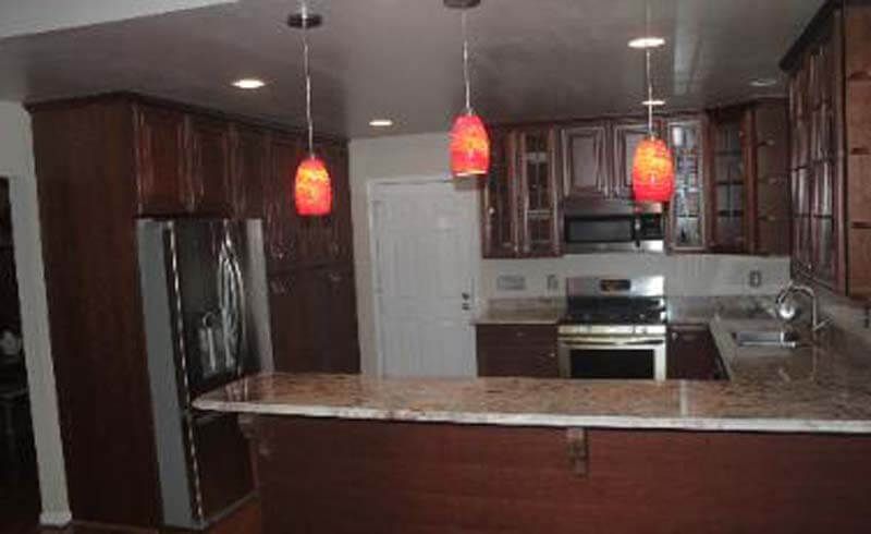 Kitchen with dark brown cabinets, granite countertops, and three hanging orange pendant lights.