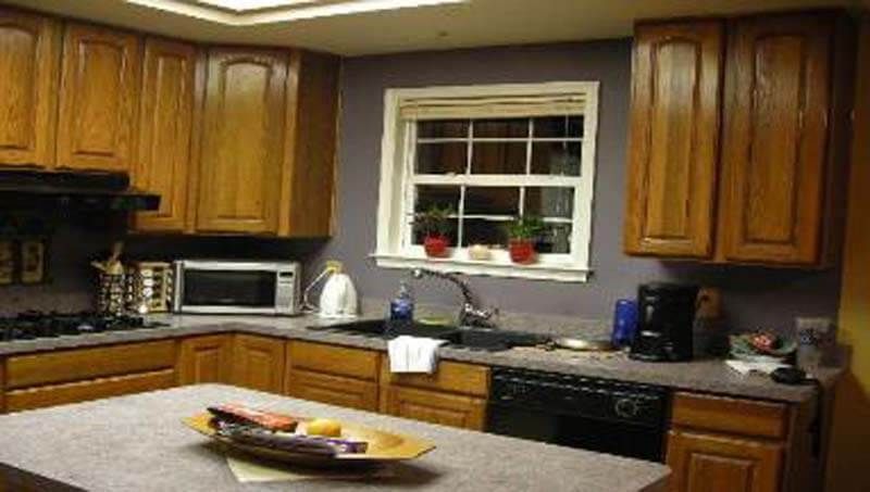 Kitchen with wood cabinets, countertop, sink, and window. Black appliances. Purple wall.