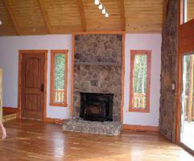 Living room with stone fireplace, wood floors, door and windows.