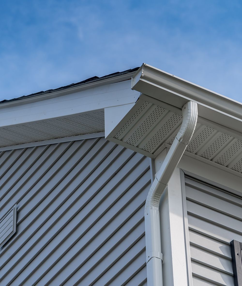 White gutter system on a house with gray siding under a blue sky.