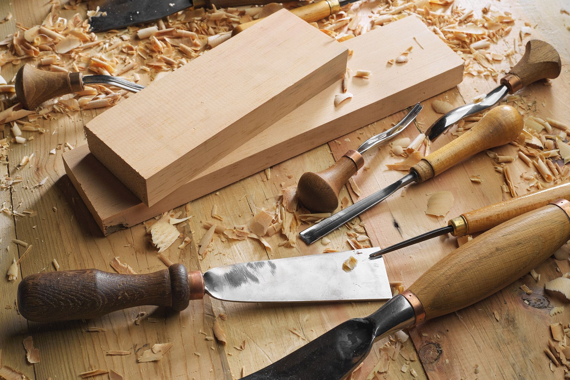 Wooden blocks with carving tools and wood shavings on a wooden surface.