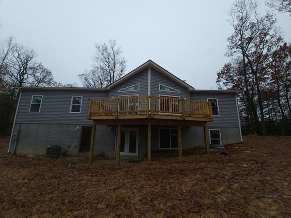 Gray house with wooden deck in a brown field under a cloudy sky.