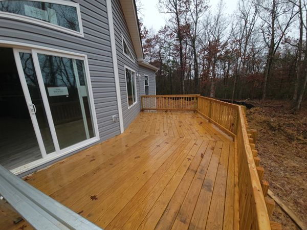 Wooden deck attached to a gray house, surrounded by trees.