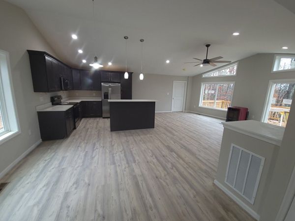 Open-concept kitchen and living area with dark cabinets, a gray island, and wood-look flooring.