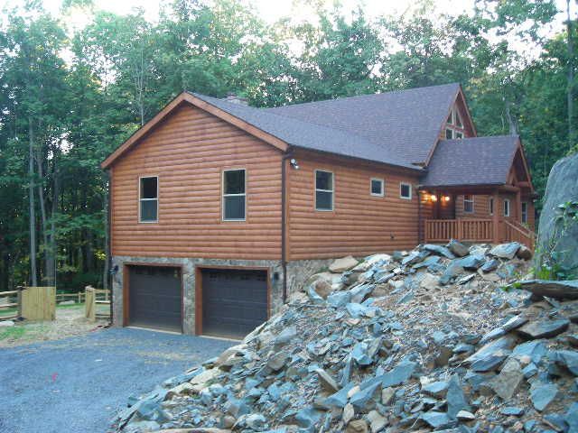Gray house with propane tanks on a grassy hillside under a blue sky.