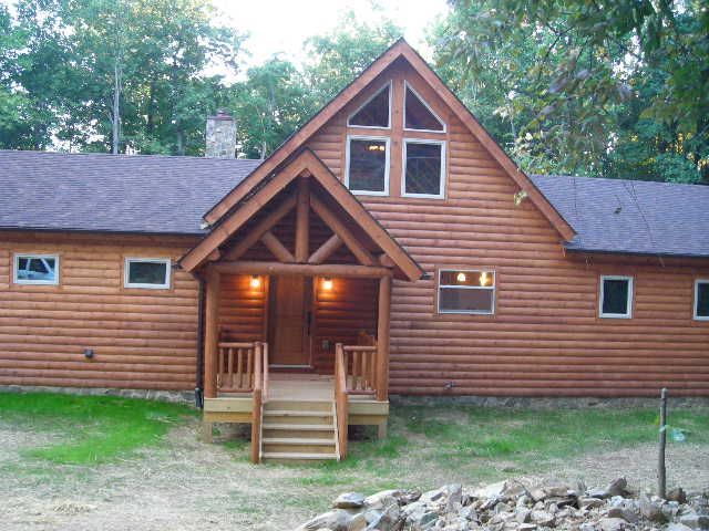 Log cabin with a porch and steps, brown siding, small windows, green grass.