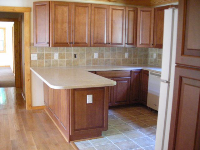 Kitchen with light-colored countertops, brown cabinets, tile backsplash, and wood flooring.