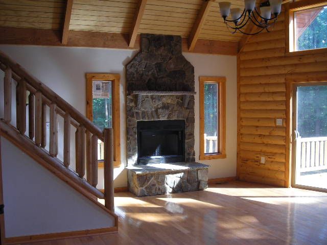 Interior of a log cabin with a stone fireplace, wooden floors, and a staircase.