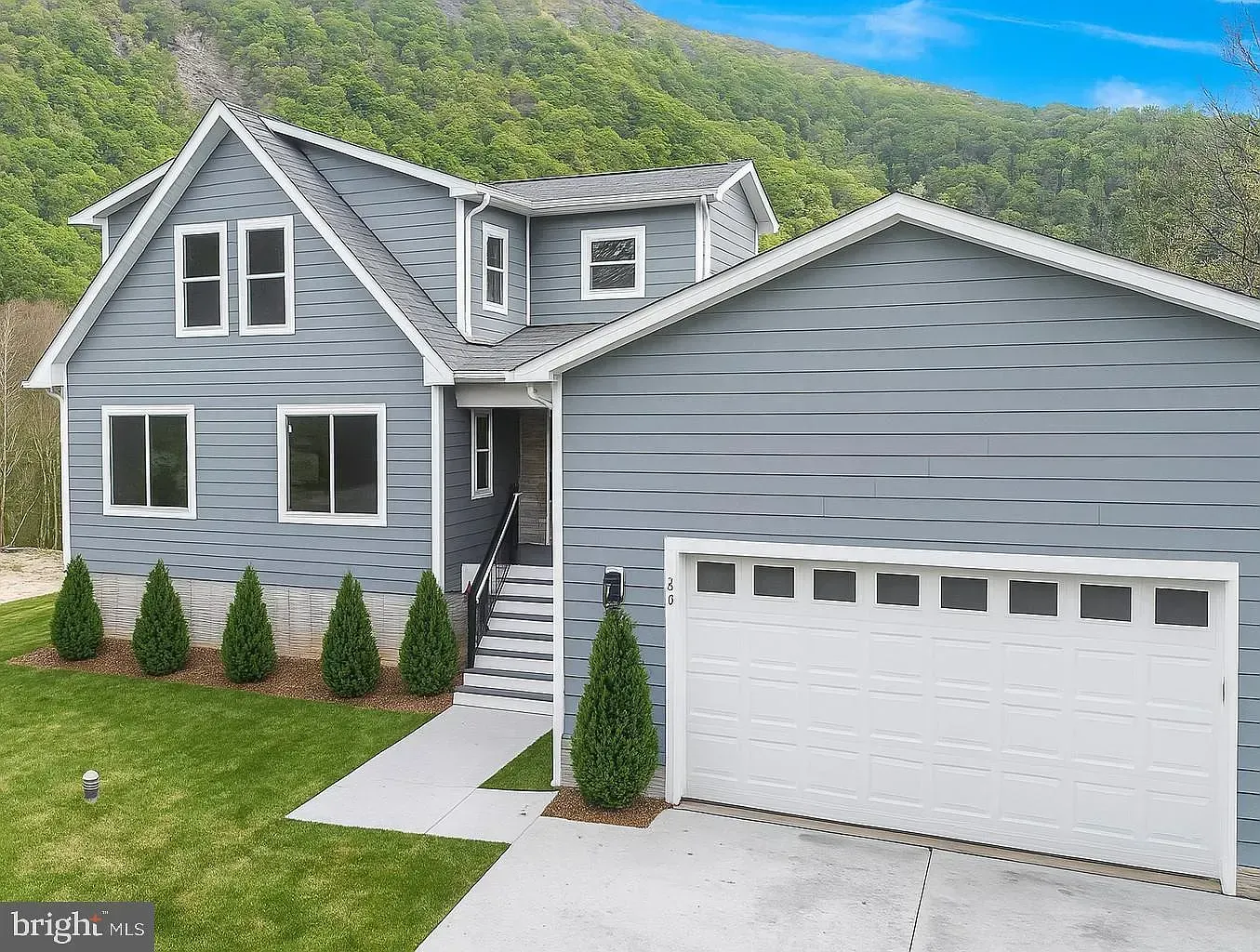 Blue house with a white garage door, nestled against a hillside.