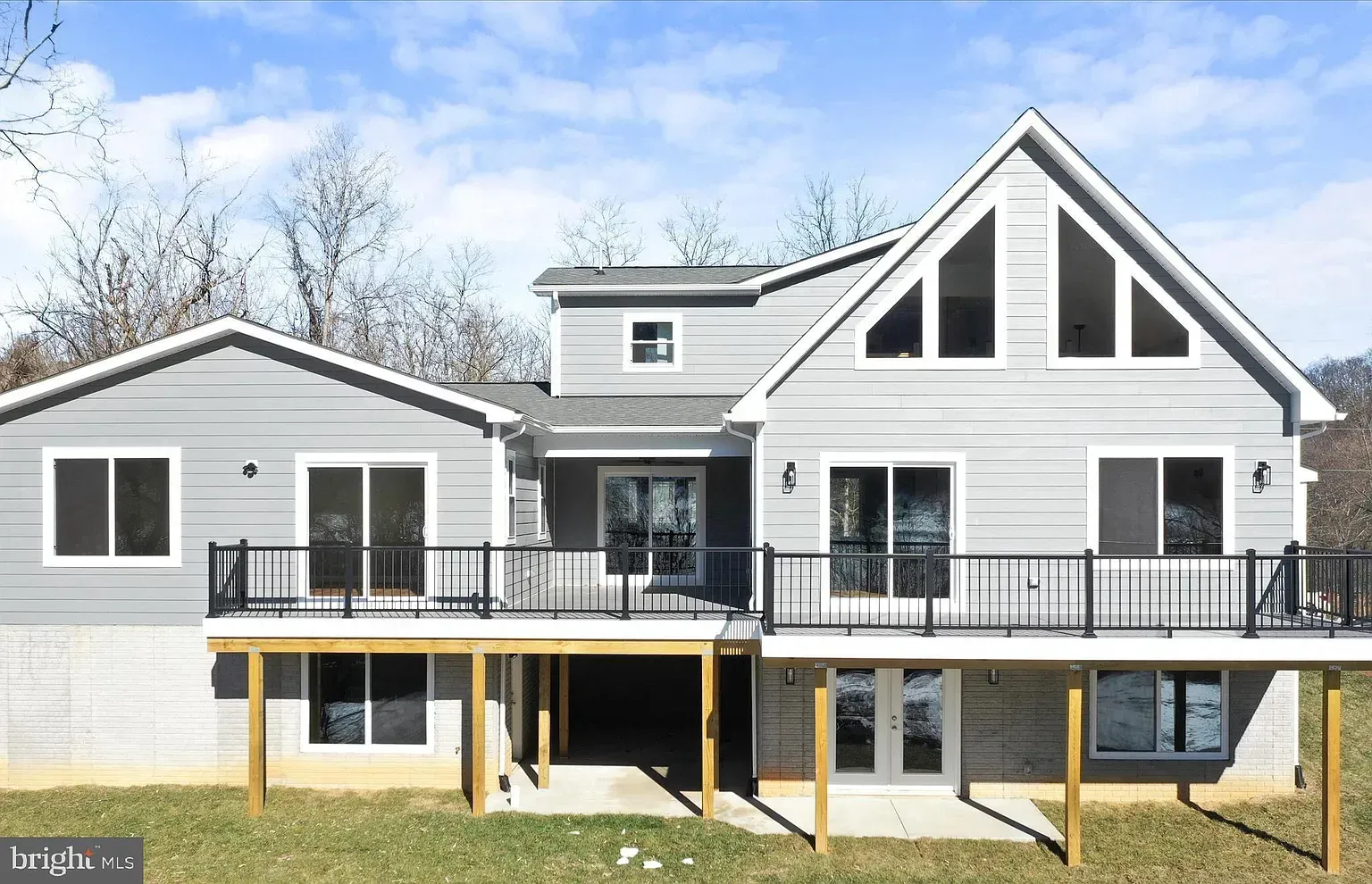 Gray house with black railings and large windows, on a grassy hill with a blue sky background.