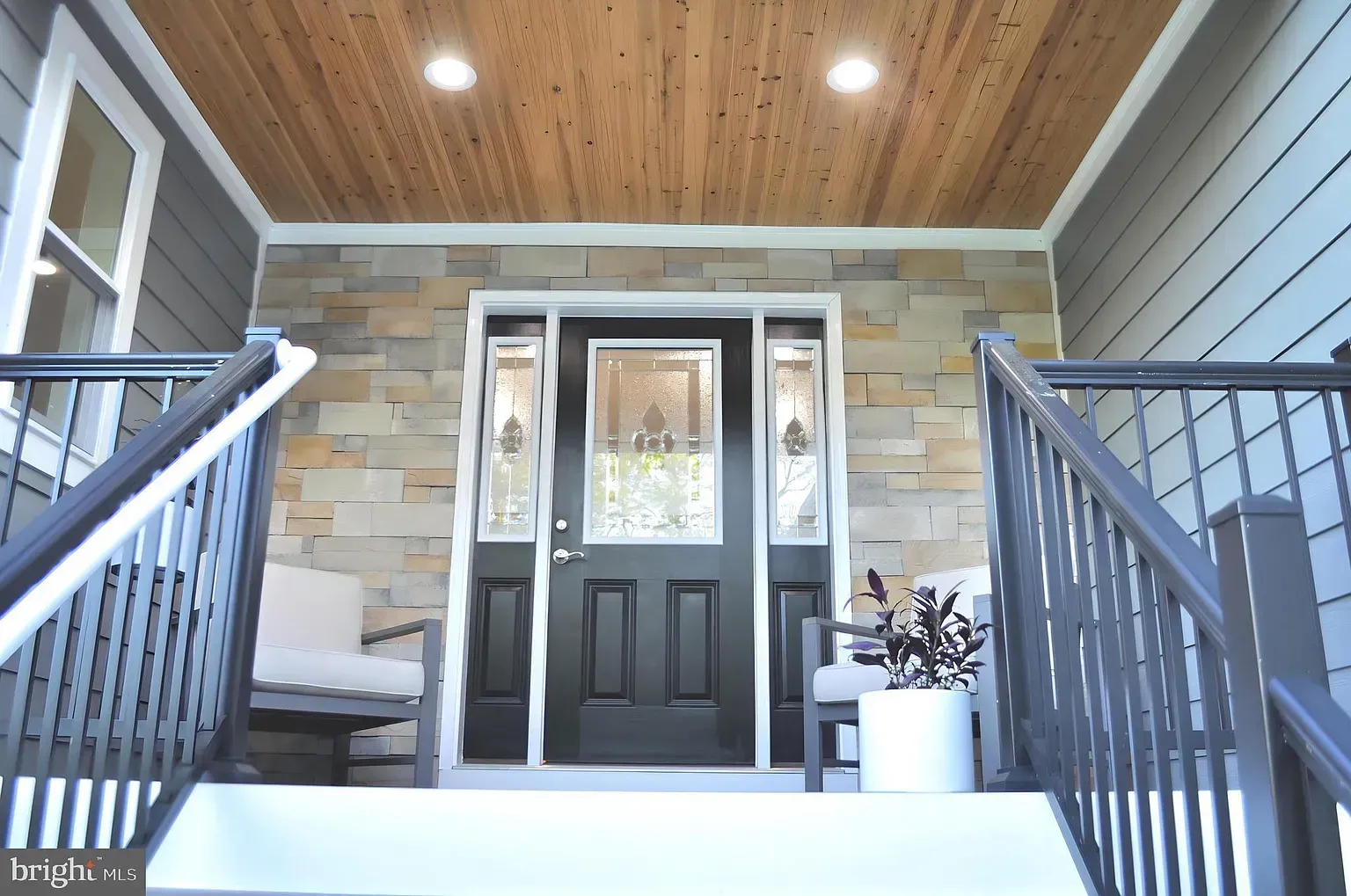 Front exterior of a house with stone accents, a dark door, and a wooden ceiling.