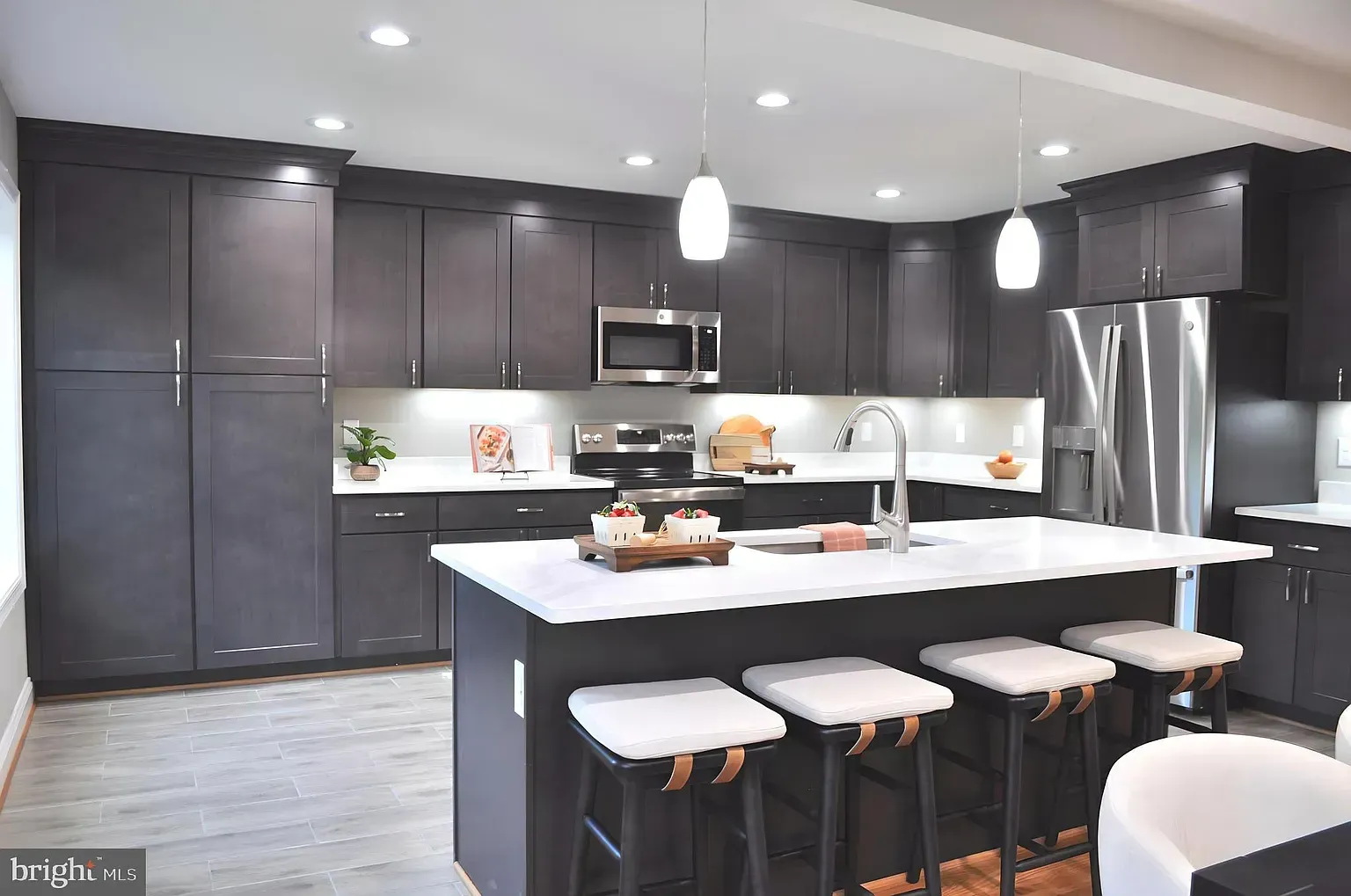 Modern kitchen with dark gray cabinets, white countertops, island with seating, stainless steel appliances.