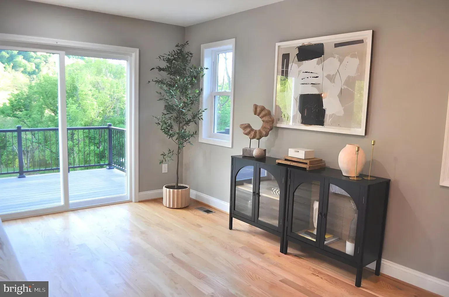 Room with sliding glass door to deck, wooden floor, black cabinet, and abstract art on the wall.