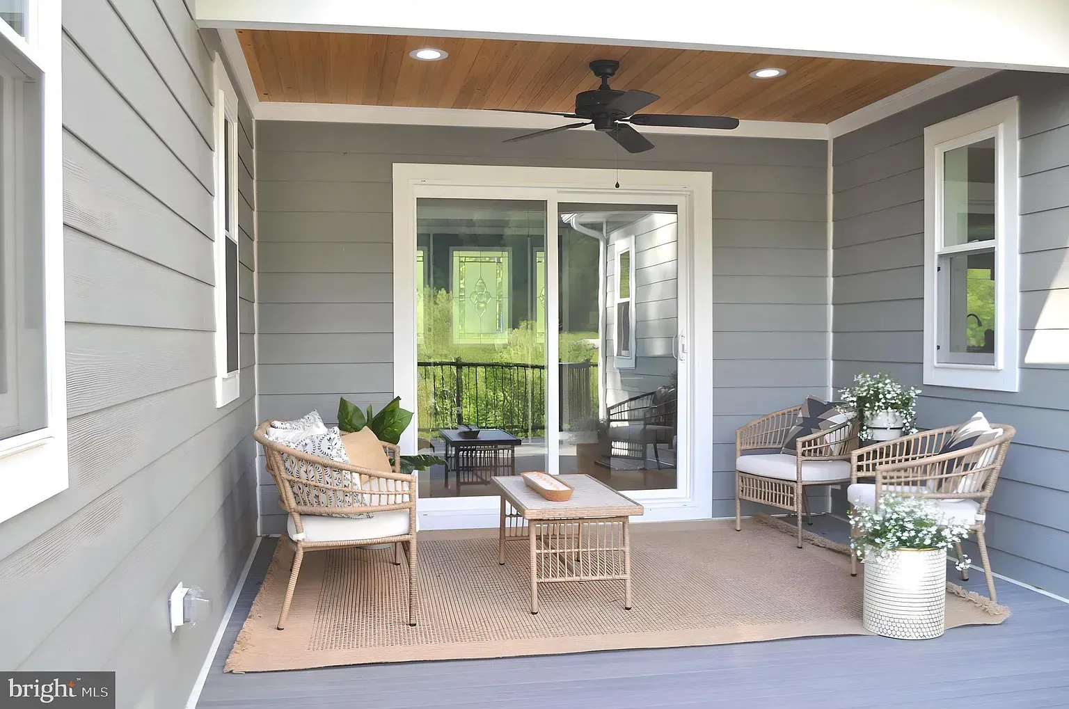 Covered outdoor patio with wicker furniture, sliding glass door, and wooden ceiling.