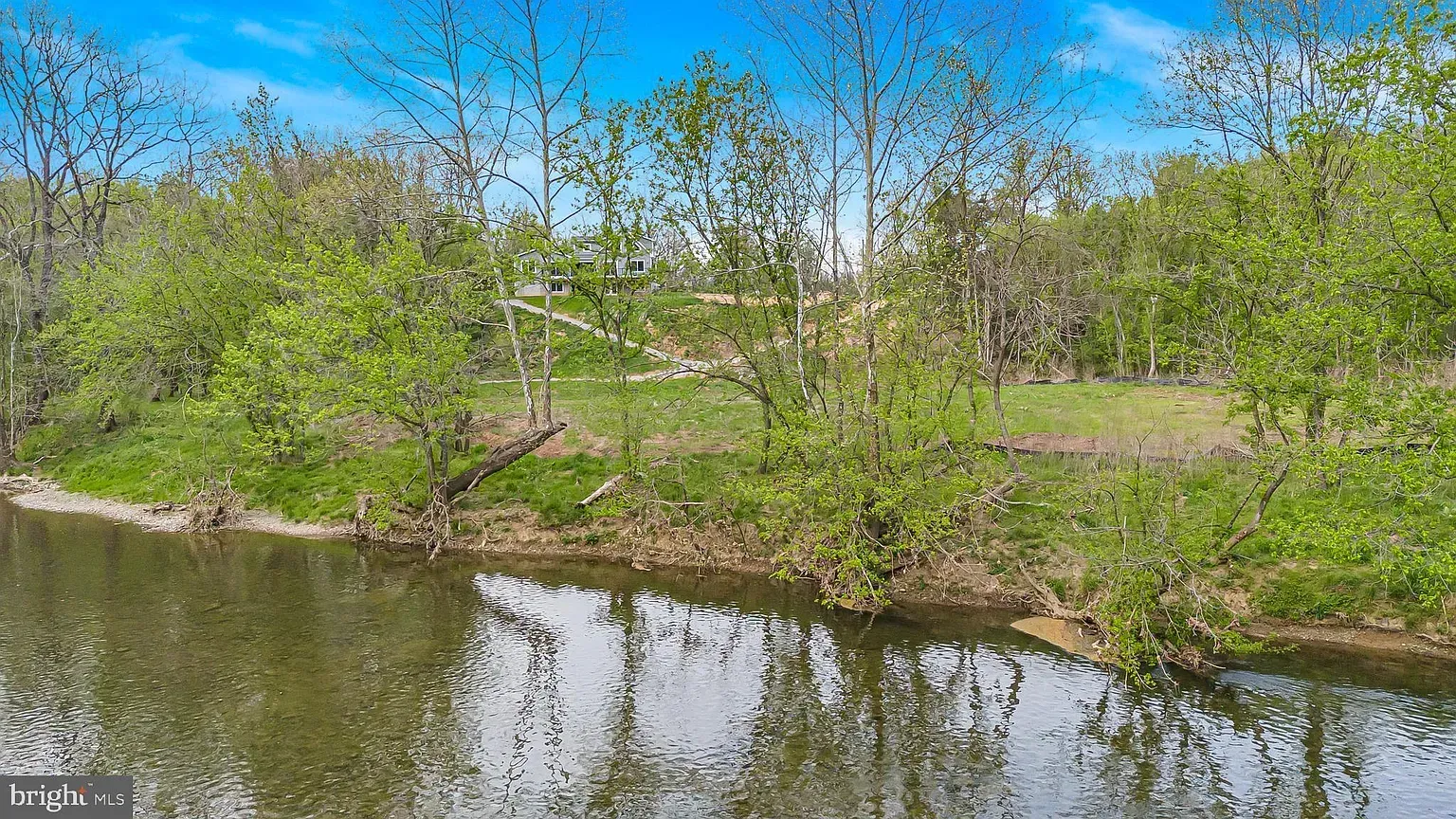 A calm river flows along a tree-lined bank under a blue sky.