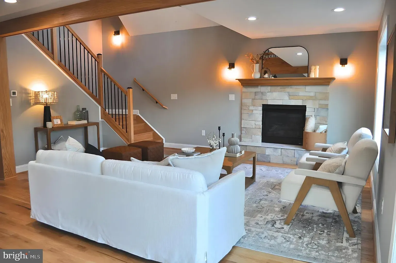 Living room with stone fireplace, wooden staircase, and white sofa.