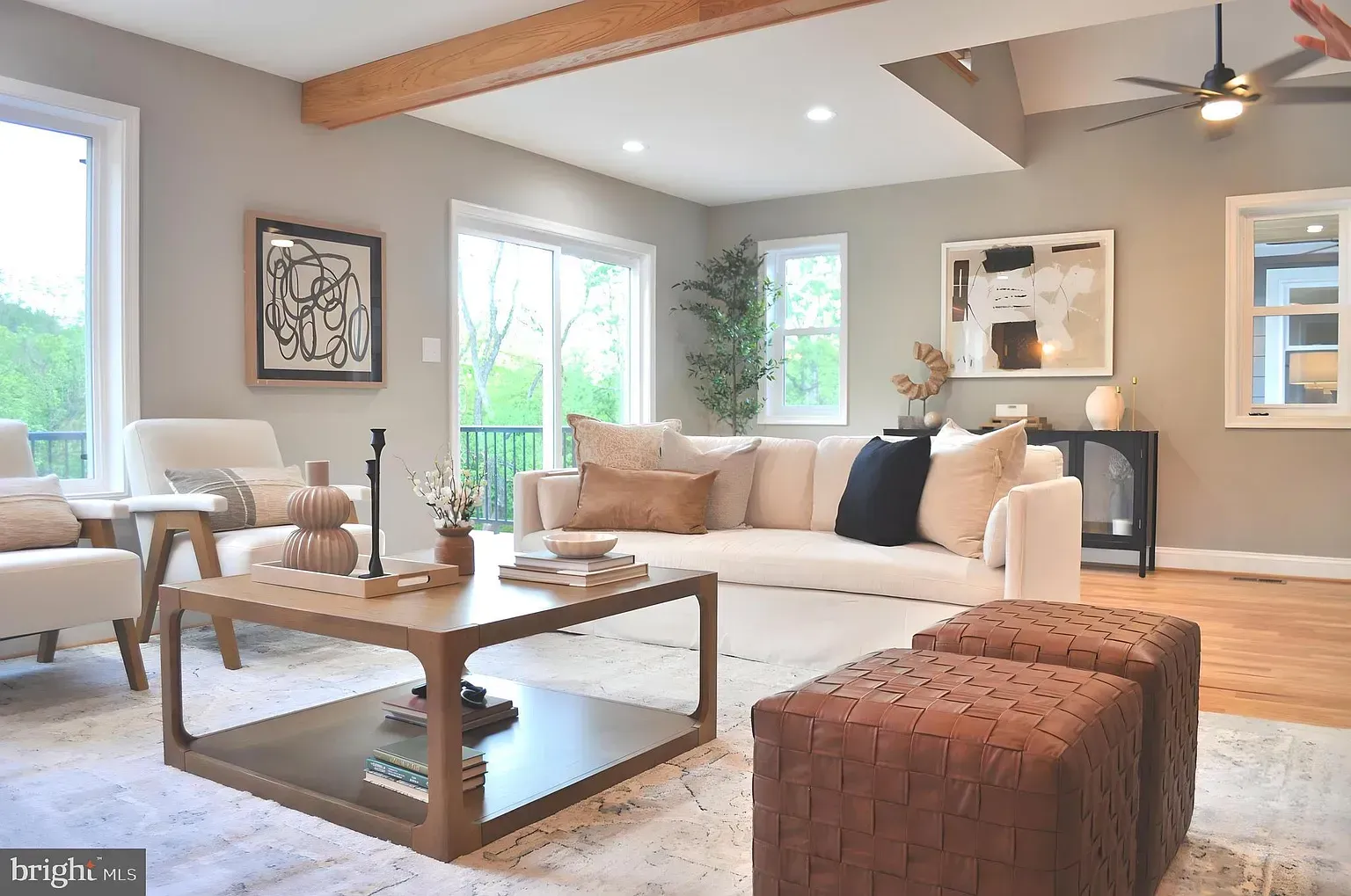 Living room with beige furniture, wooden accents, and a large window overlooking trees.