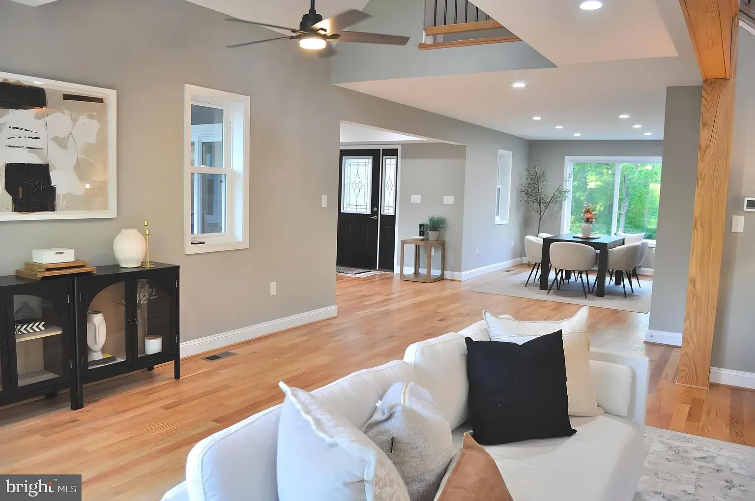 Living room with white sofa, wood floors, neutral walls, and dining area in the background.