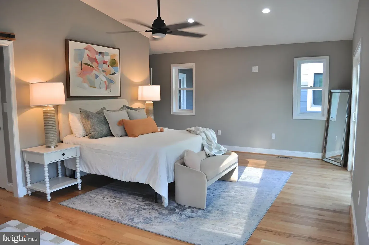 Bedroom with a bed, nightstands, rug, windows, and a ceiling fan. Neutral color scheme with light wood flooring.