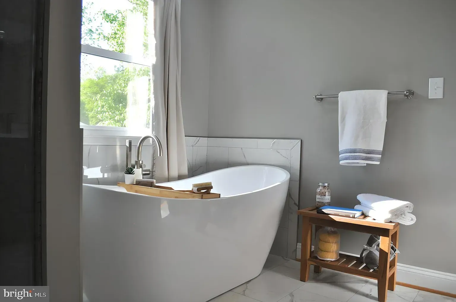 Modern bathroom with a white freestanding tub, gray walls, and a small wooden shelf.