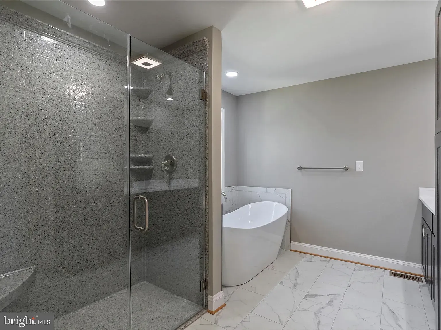 Modern bathroom with a glass shower, soaking tub, and gray walls. Marble floors.