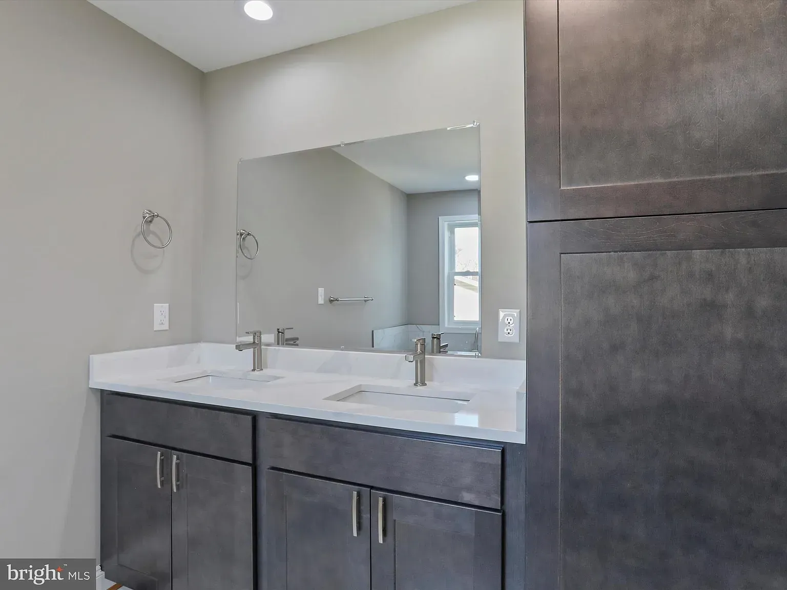 Bathroom with double sink vanity, large mirror, and gray cabinetry.