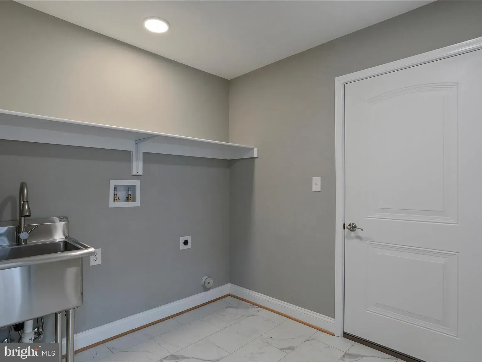 Laundry room with a stainless steel sink, white shelf, gray walls, and white door.