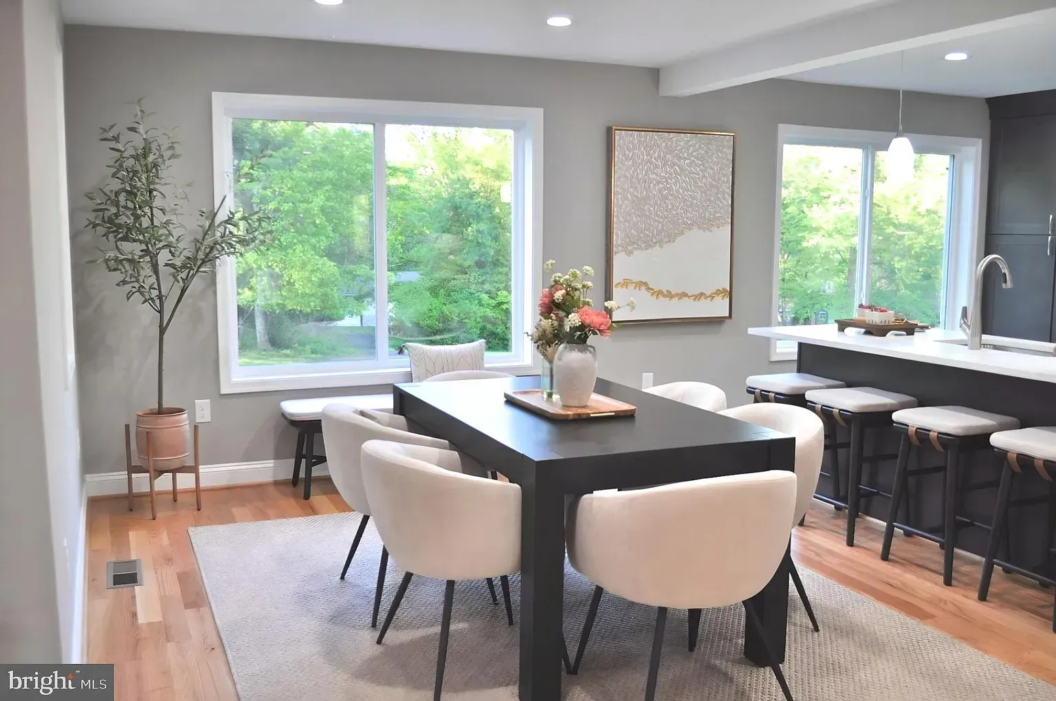 Dining room with black table, white chairs, large windows, and a rug.