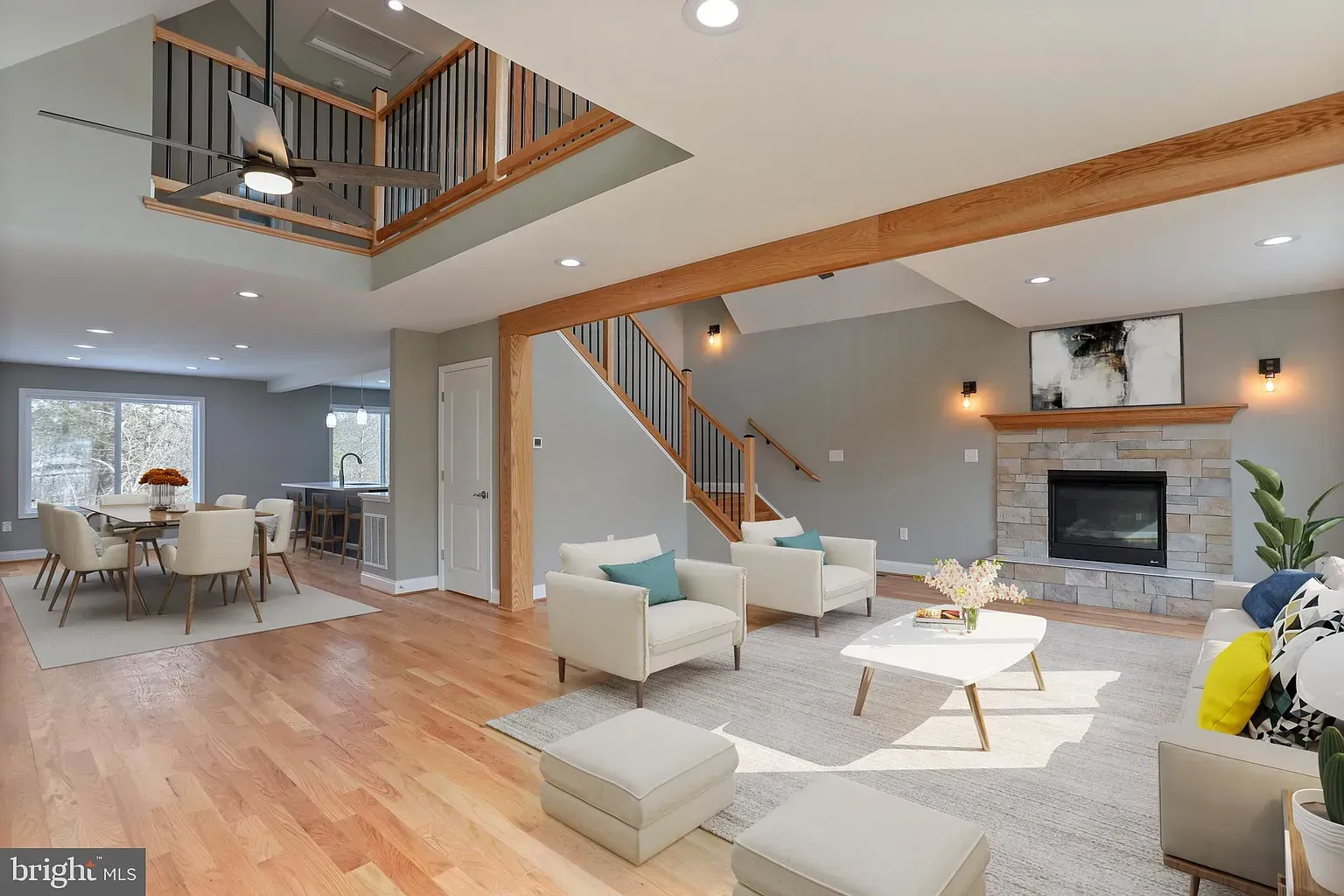 Spacious living room with hardwood floors, fireplace, and staircase. Light-colored walls and furniture.