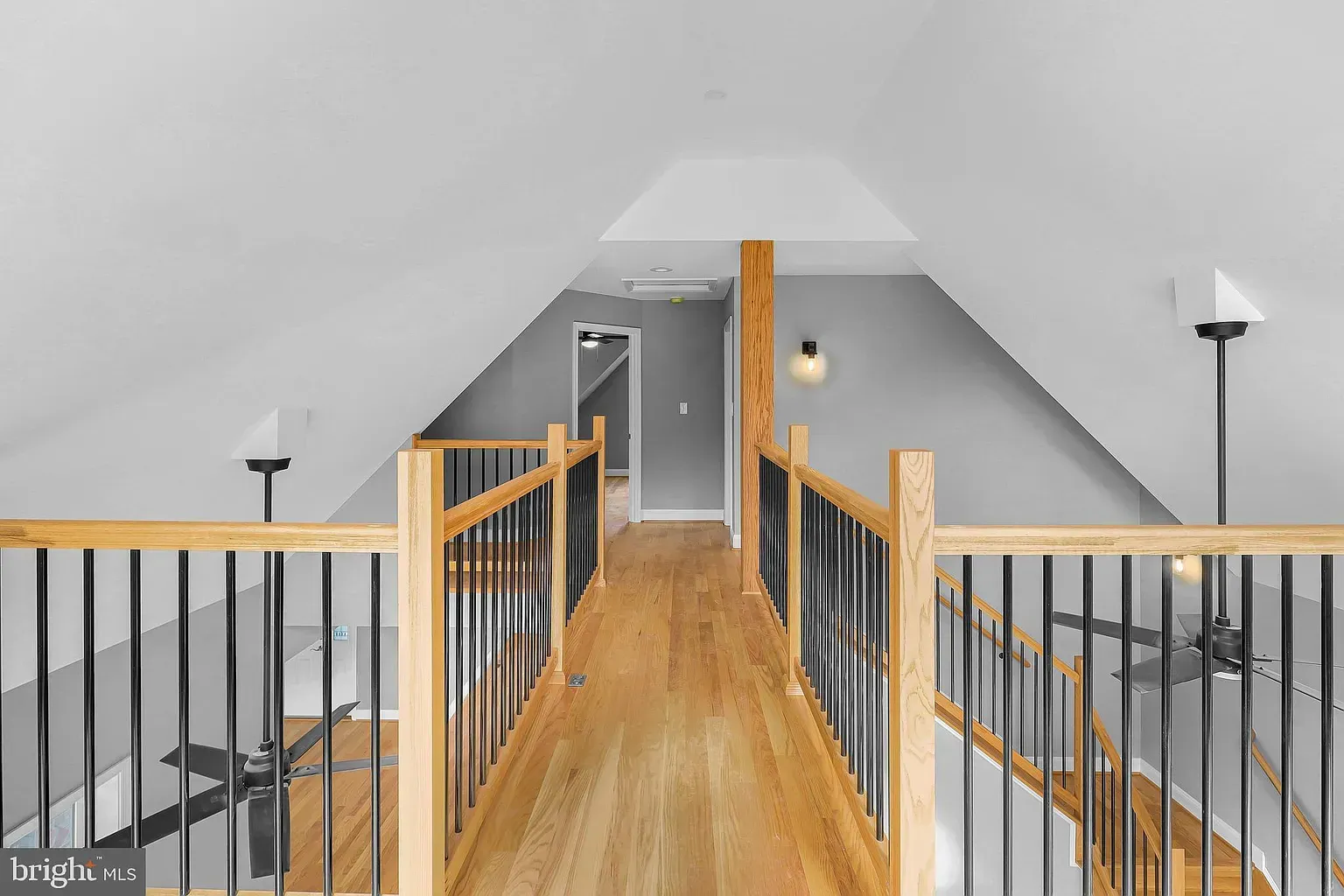 Wooden walkway in an attic with railings, leading to a doorway, gray and white walls.