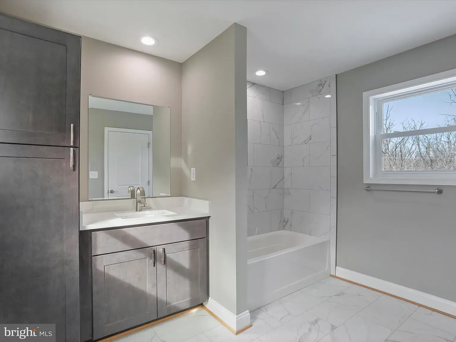 Modern gray bathroom with vanity, bathtub, and window; white tile, wood trim.