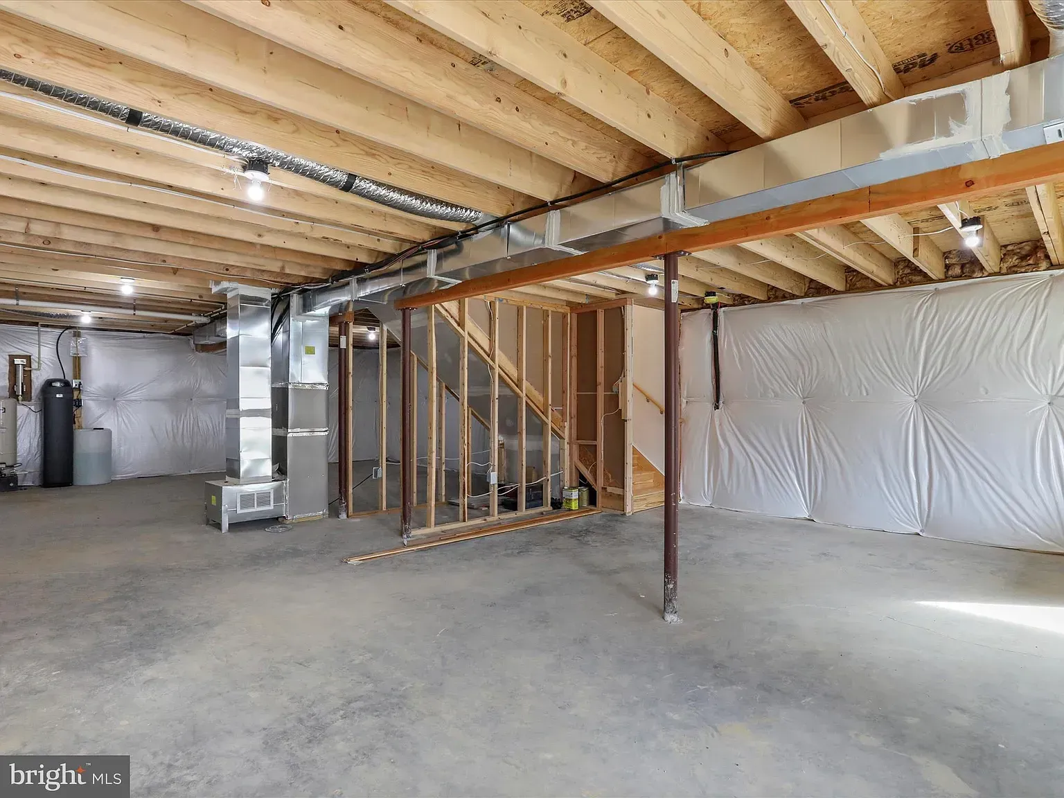 Unfinished basement with concrete floor, exposed wooden beams, and insulation on the walls.