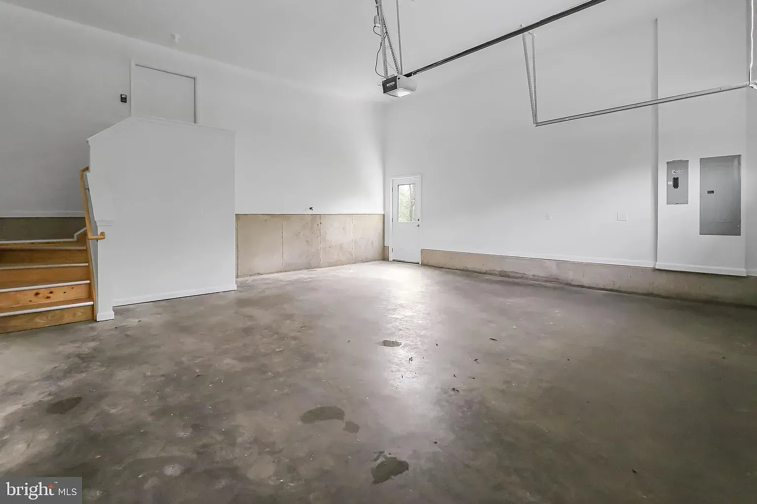 Empty garage with concrete floor, white walls, and stairs on the left.