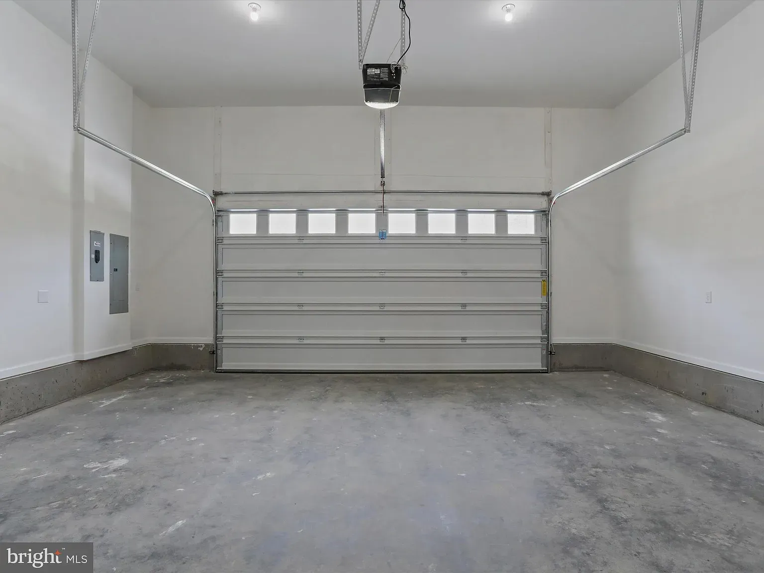 Empty, freshly-painted garage with closed white door, concrete floor, and overhead lights.