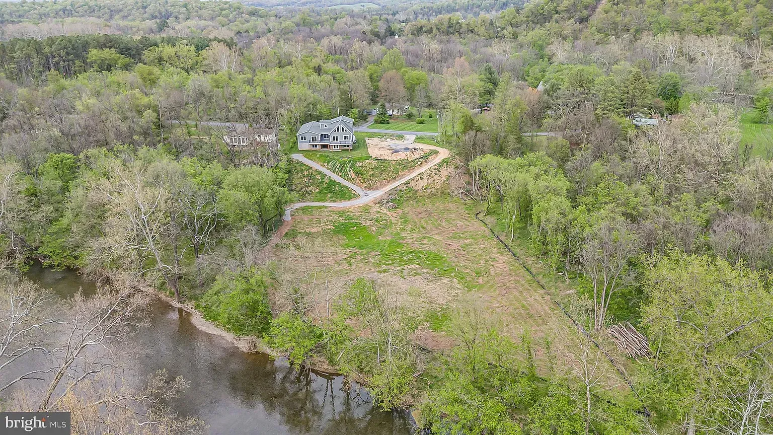 Aerial view of a house on a hillside above a river, surrounded by trees.
