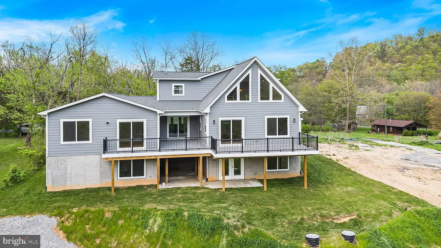 Gray house with deck on a grassy hill. Trees in background, sunny day.