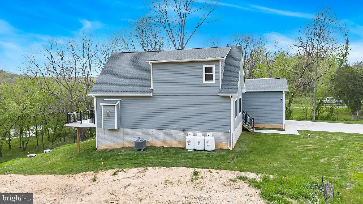 Gray house with detached garage on a grassy hill under a blue sky. Three propane tanks are in front.