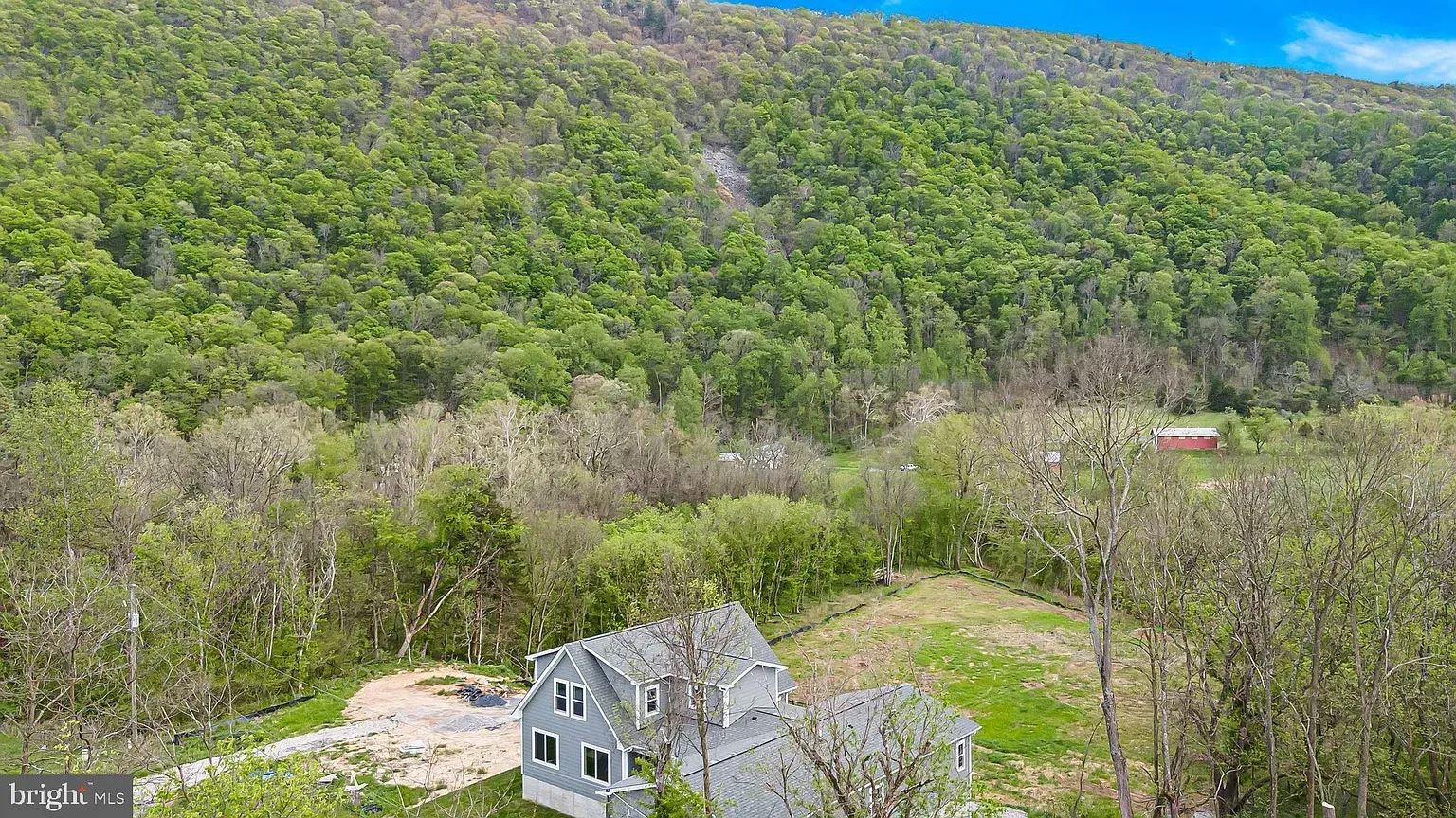 House nestled near a lush, forested mountain, blue sky overhead.