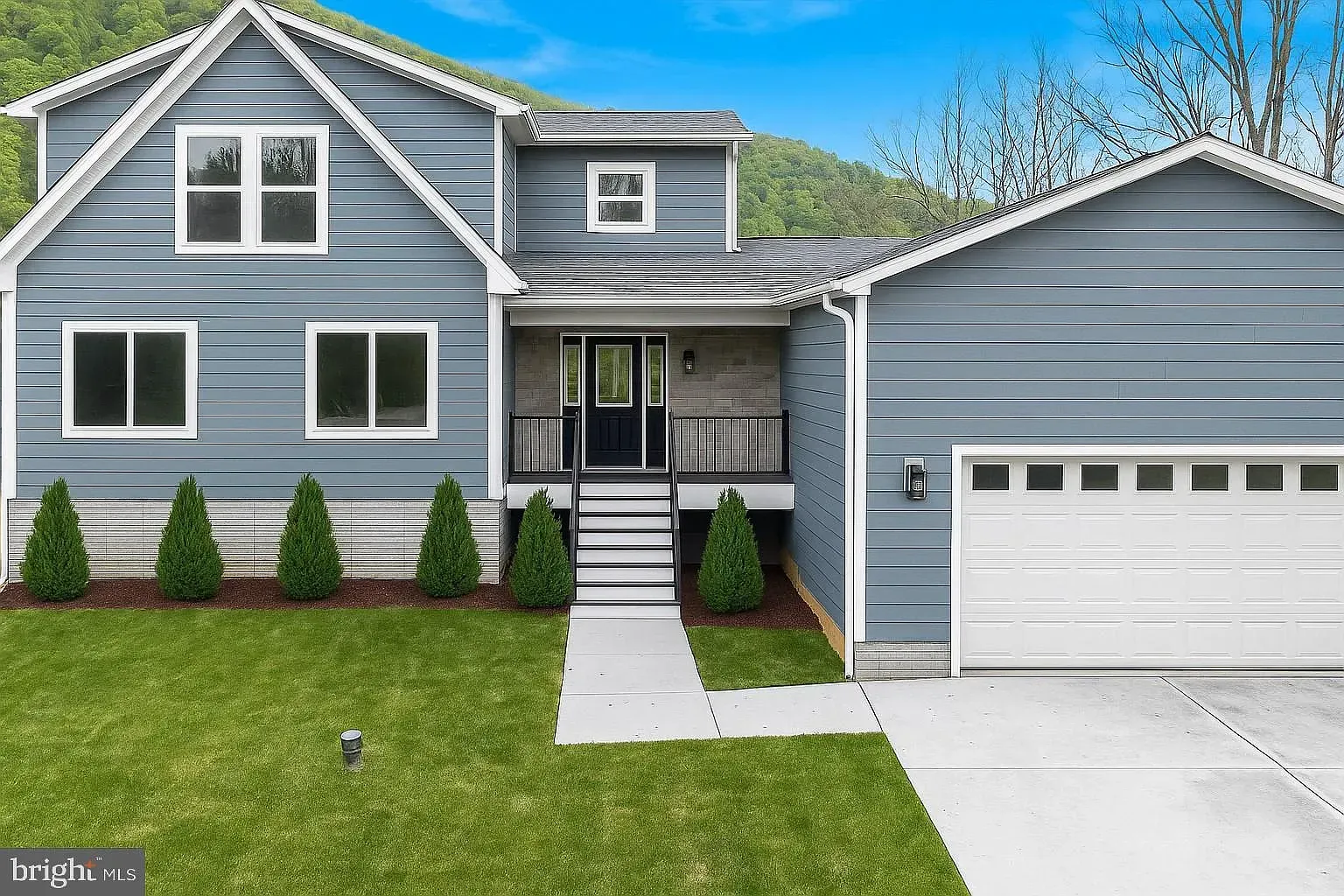 Blue house with white trim, garage, front porch with stairs, and small trees on a green lawn.