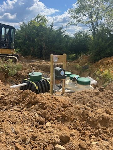 Excavation site with septic tank components, including green lids, electrical box, and backhoe.