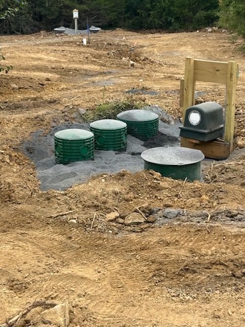 Septic system components installed in a dirt clearing; four green lids, a black electrical box, and a wooden frame.