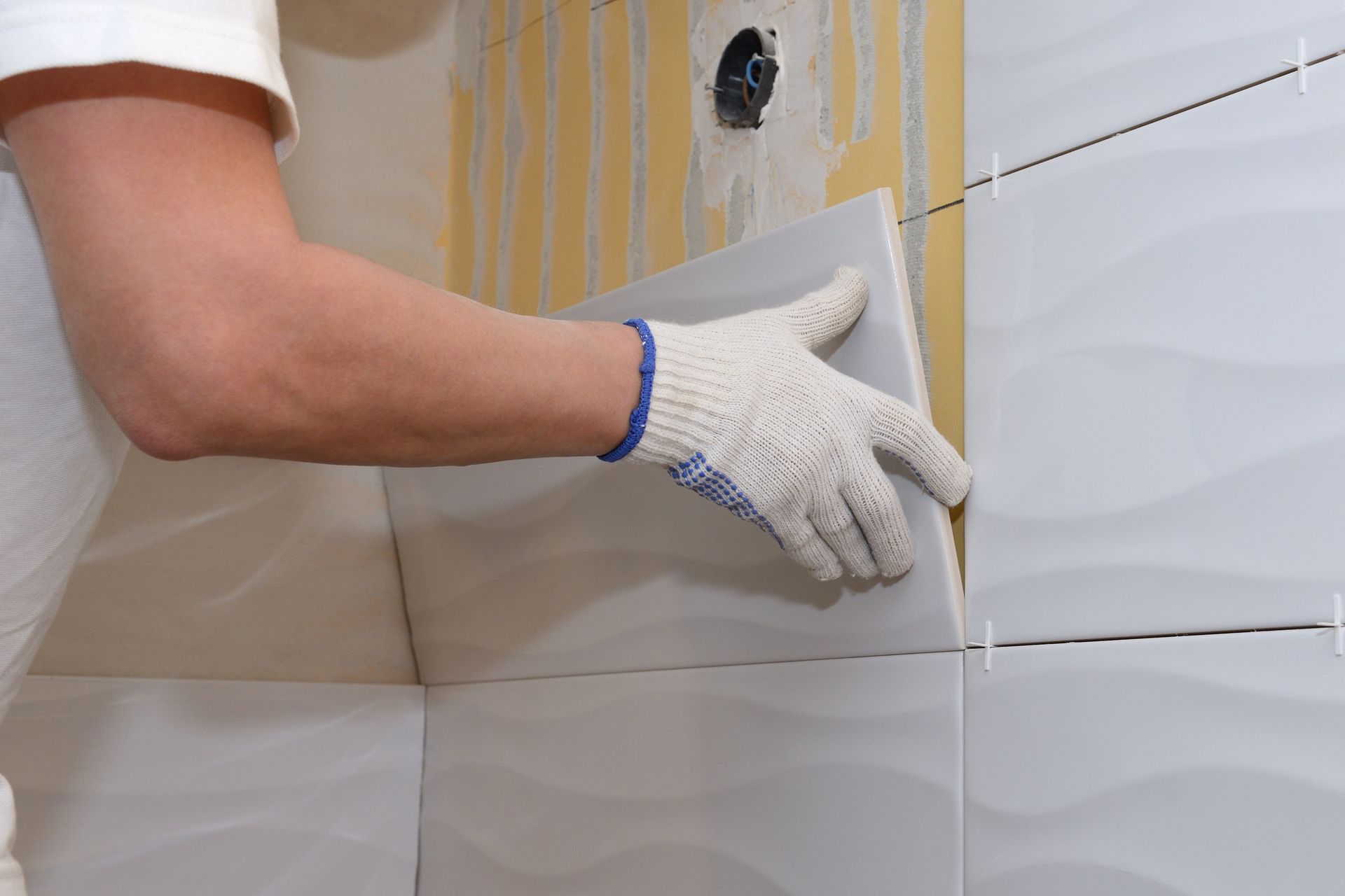 A man wearing gloves is installing tiles on a wall.