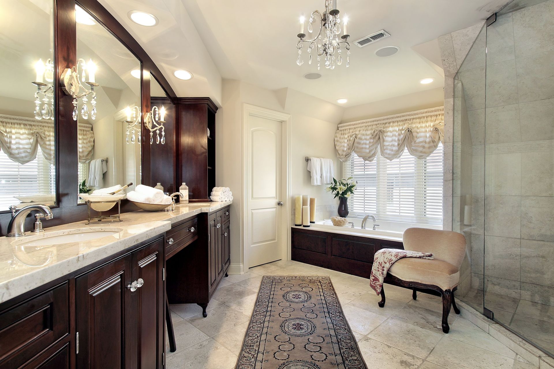 A bathroom with two sinks , a chair , a tub and a chandelier.