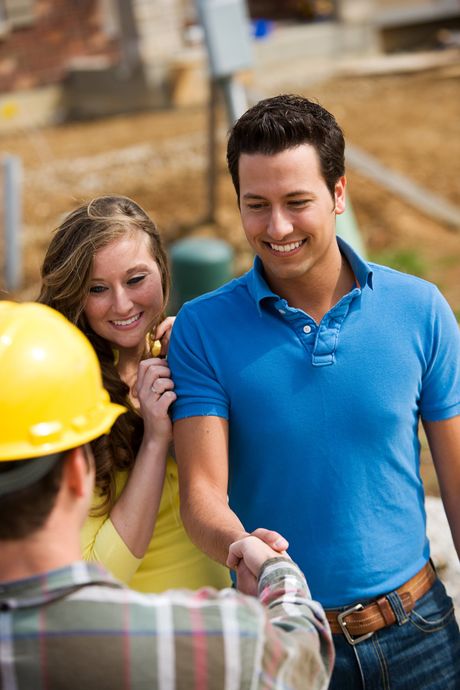 A man and woman are shaking hands with a construction worker at a construction site.