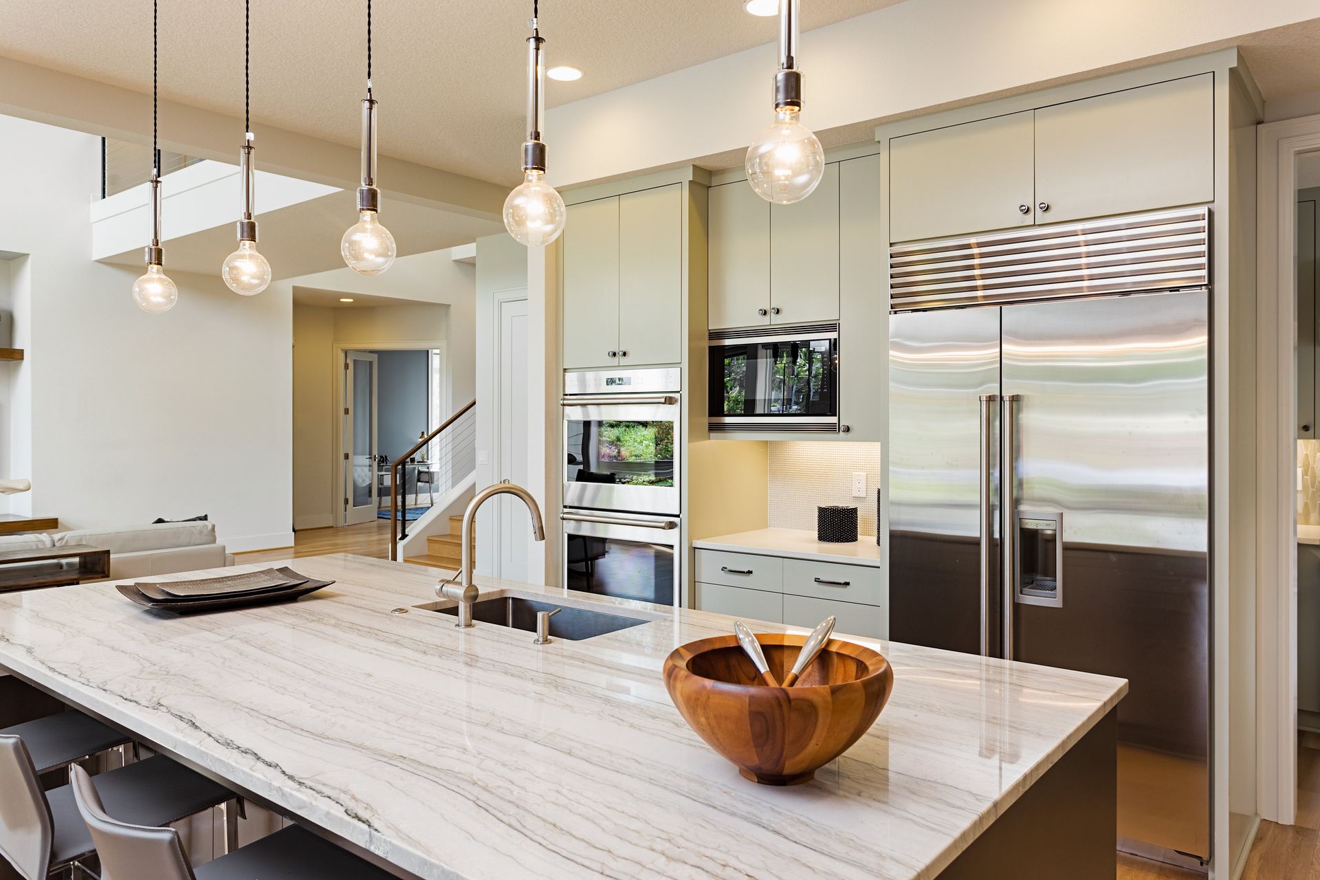A kitchen with a marble counter top , stainless steel appliances , and a wooden bowl on the counter.