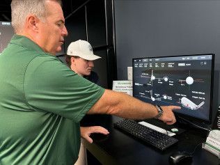 A man is pointing at a computer screen while a woman looks on.