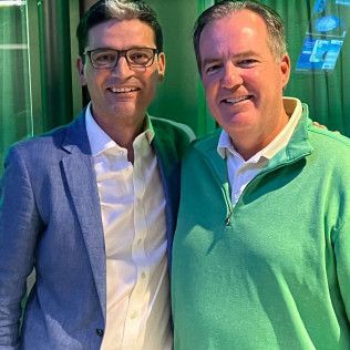 Two men are posing for a picture together in front of a green curtain.