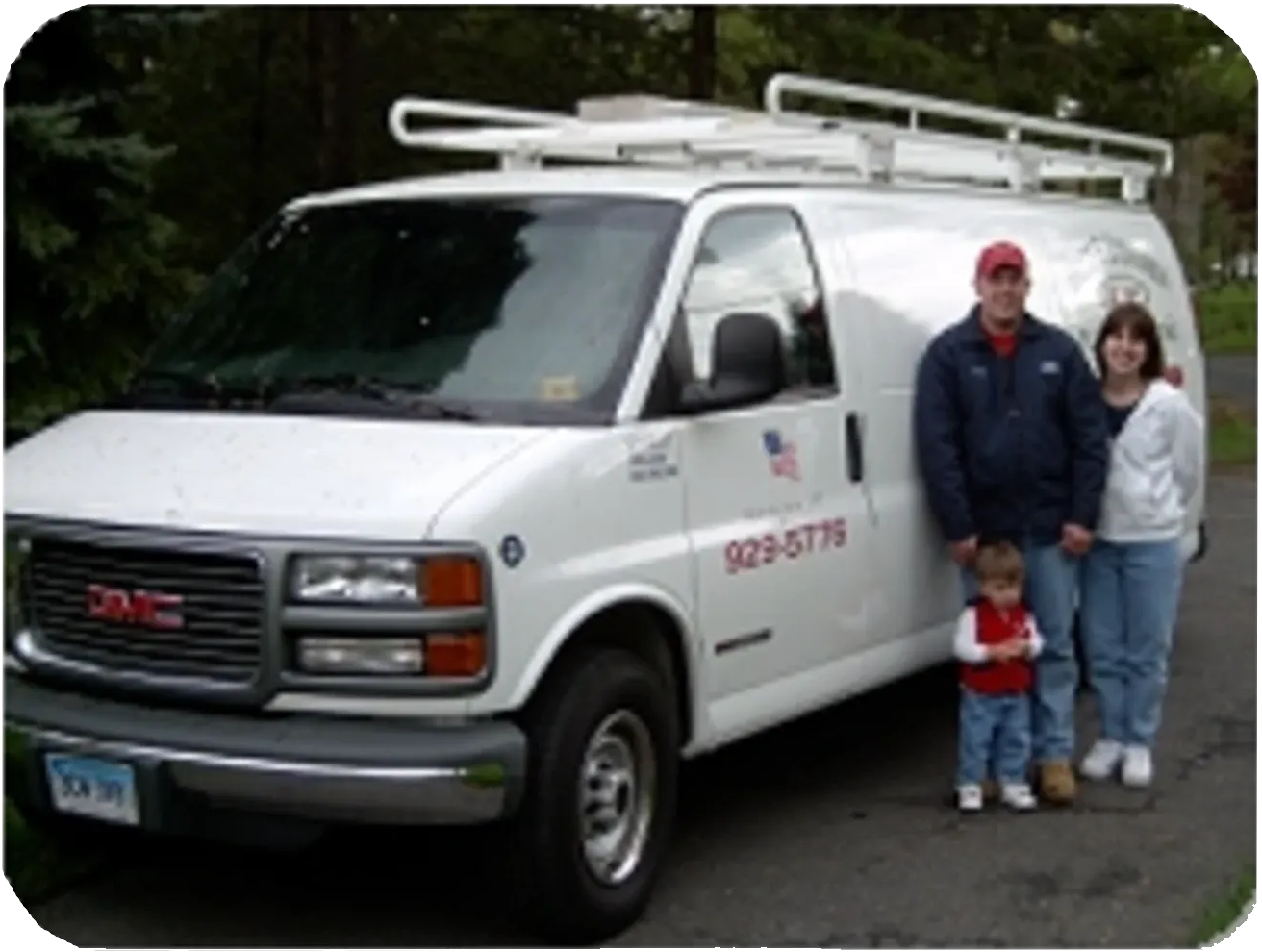 Family standing next to a white service van with a roof rack; smiling, sunny.